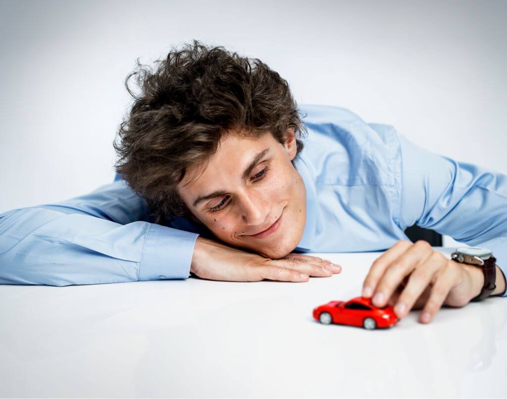 Young man in blue shirt playing with red toy car.