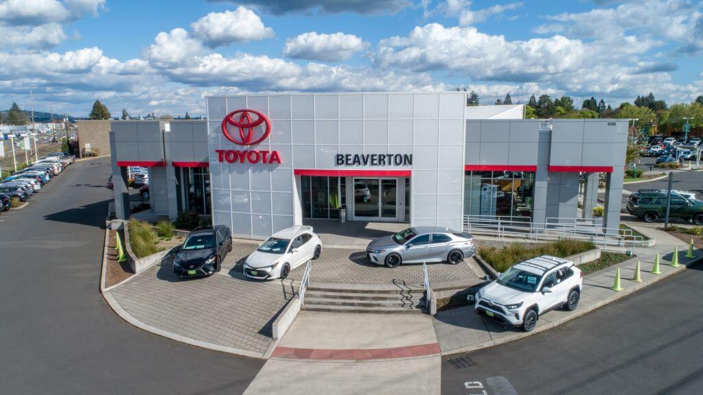 Front of Beaverton Toyota building with new Toyotas parked in front.