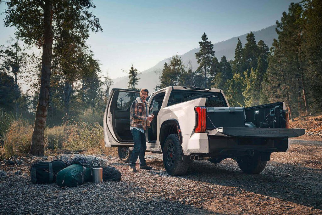 White Toyota Tundra in wilderness with man and camping gear next to truck.