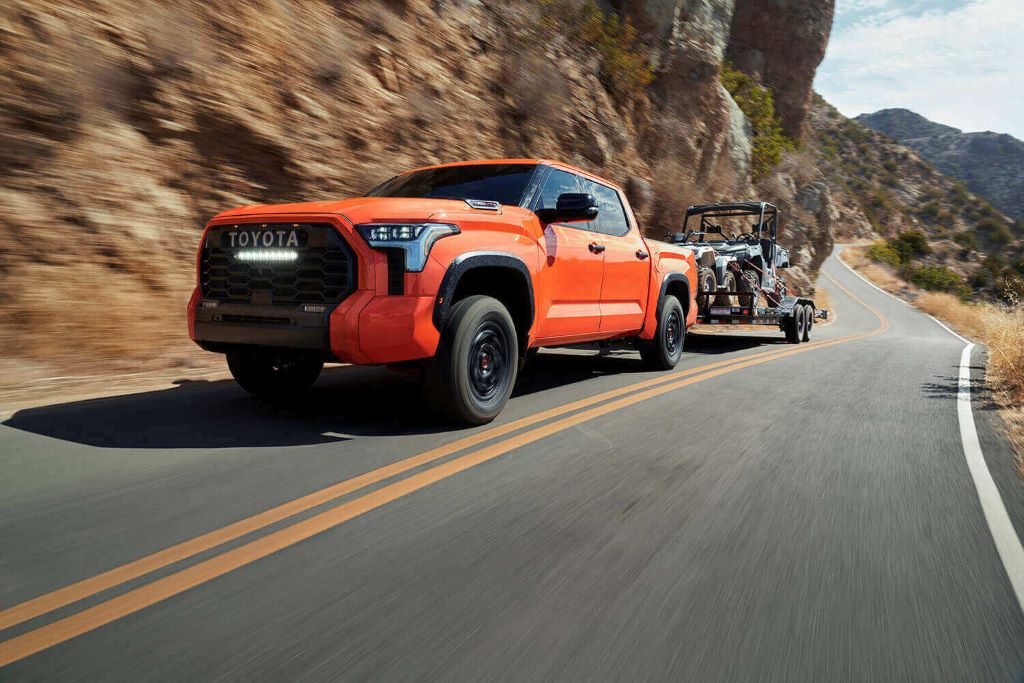 Orange Toyota Tundra towing a trailer with an ATV on a highway.