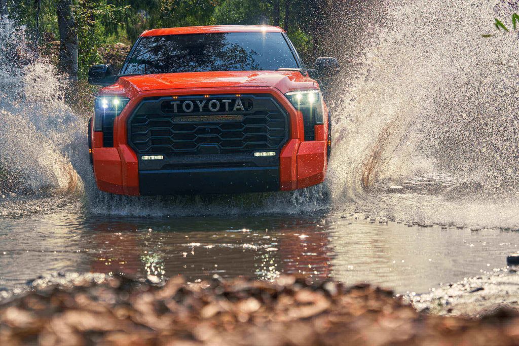 Orange Toyota Tundra driving through a mud hole.